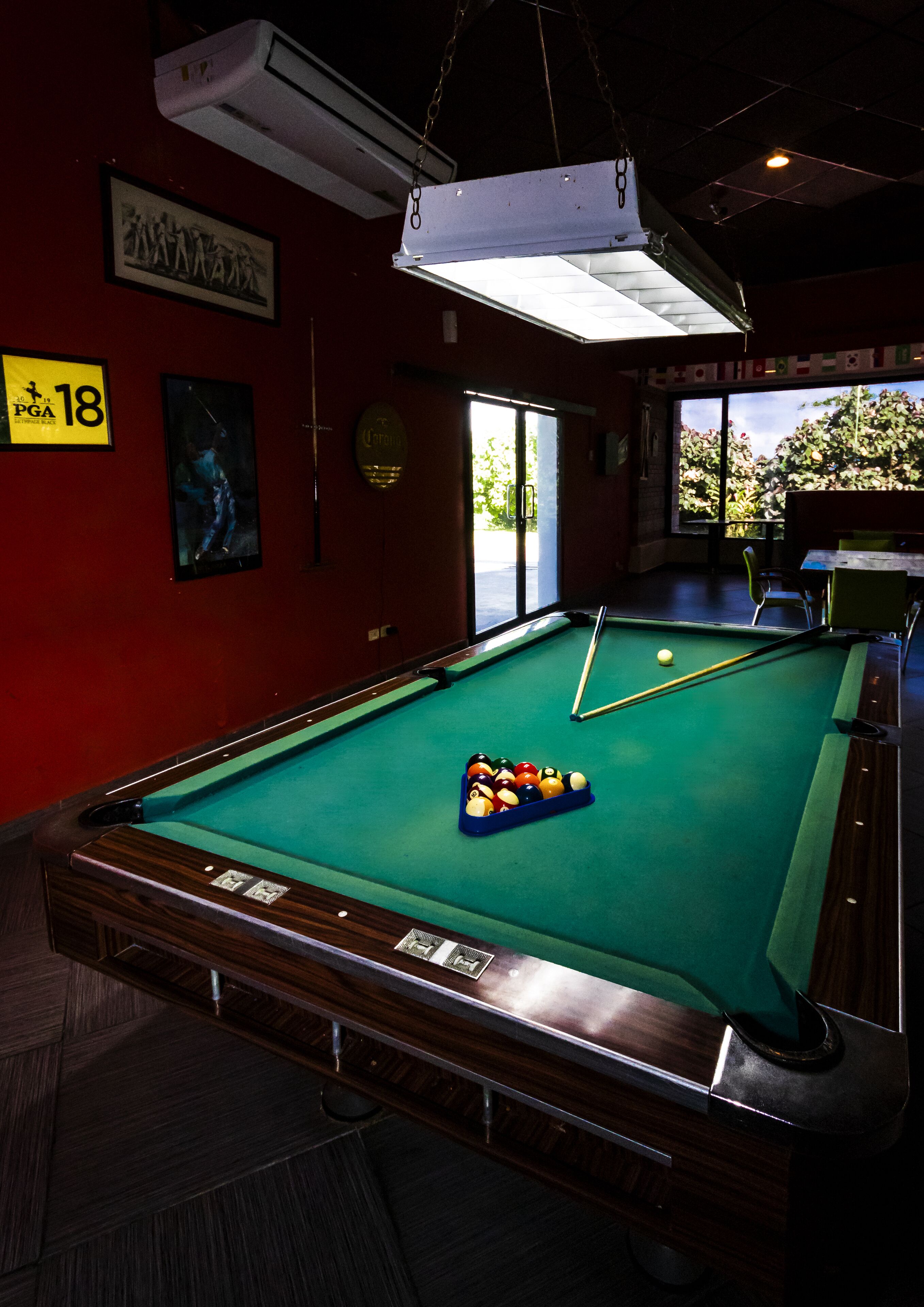 A pool table with balls, a sign indicating room number 18, and a window with a view of greenery.