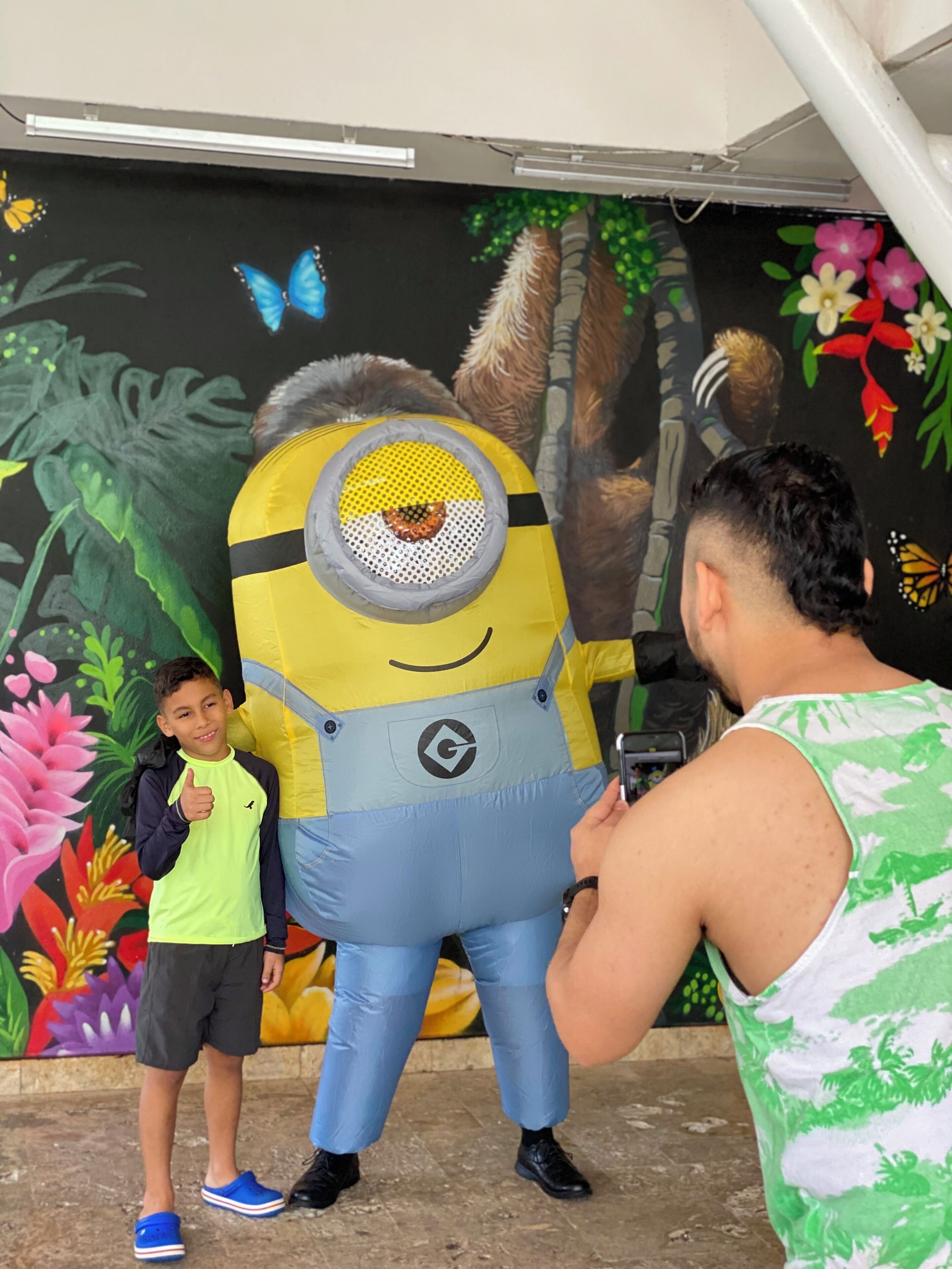 Une personne déguisée en Minion, un enfant qui lève le pouce en signe d’approbation, et un homme qui ajuste le costume.