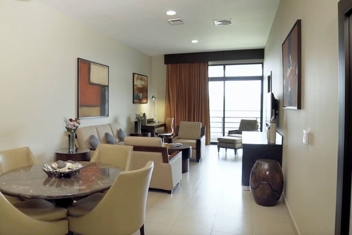 A hotel room with a dining area, a sofa, a TV, and a large window.