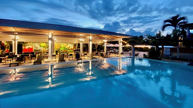 A poolside area with lounge chairs and a covered seating area, reflecting the pool and surrounding structures. - Summit Rainforest Golf Resort & All Inclusive (Panama City)