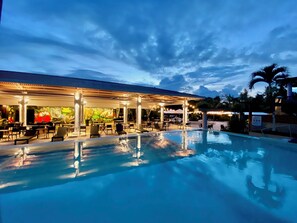 A poolside area with lounge chairs and a covered seating area, reflecting the pool and surrounding structures. - Summit Rainforest Golf Resort & All Inclusive (Panama City)