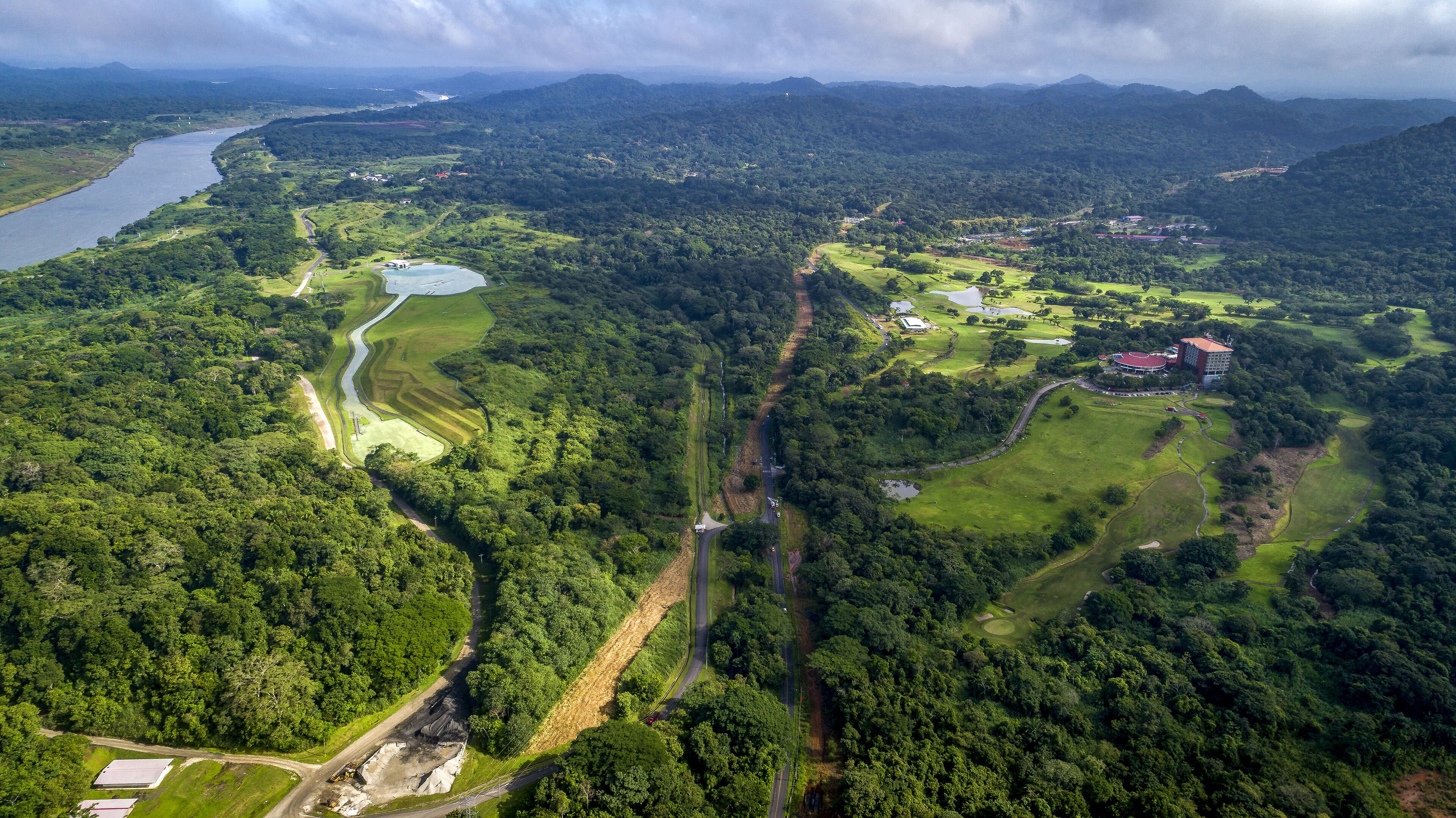 Luchtbeeld van een golfbaan met een rivier, dicht bos en een klein gebouw met een rood dak.