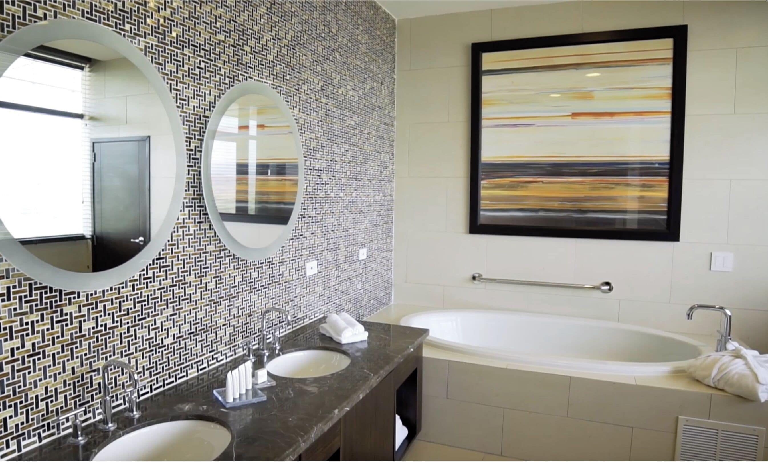 Une salle de bain avec deux lavabos, un grand miroir, une baignoire et une œuvre d’art accrochée au mur.