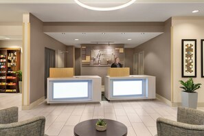 A hotel reception area with two reception desks, a large wall-mounted artwork, and a reception desk with a plant. - Holiday Inn Express & Suites Mt. Pleasant by IHG (Mount Pleasant)