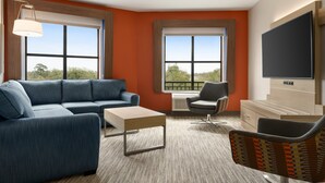 A modern living room with a sectional sofa, a coffee table, a chair, and a flat-screen TV mounted on the wall. - Holiday Inn Express & Suites Mt. Pleasant by IHG (Mount Pleasant)