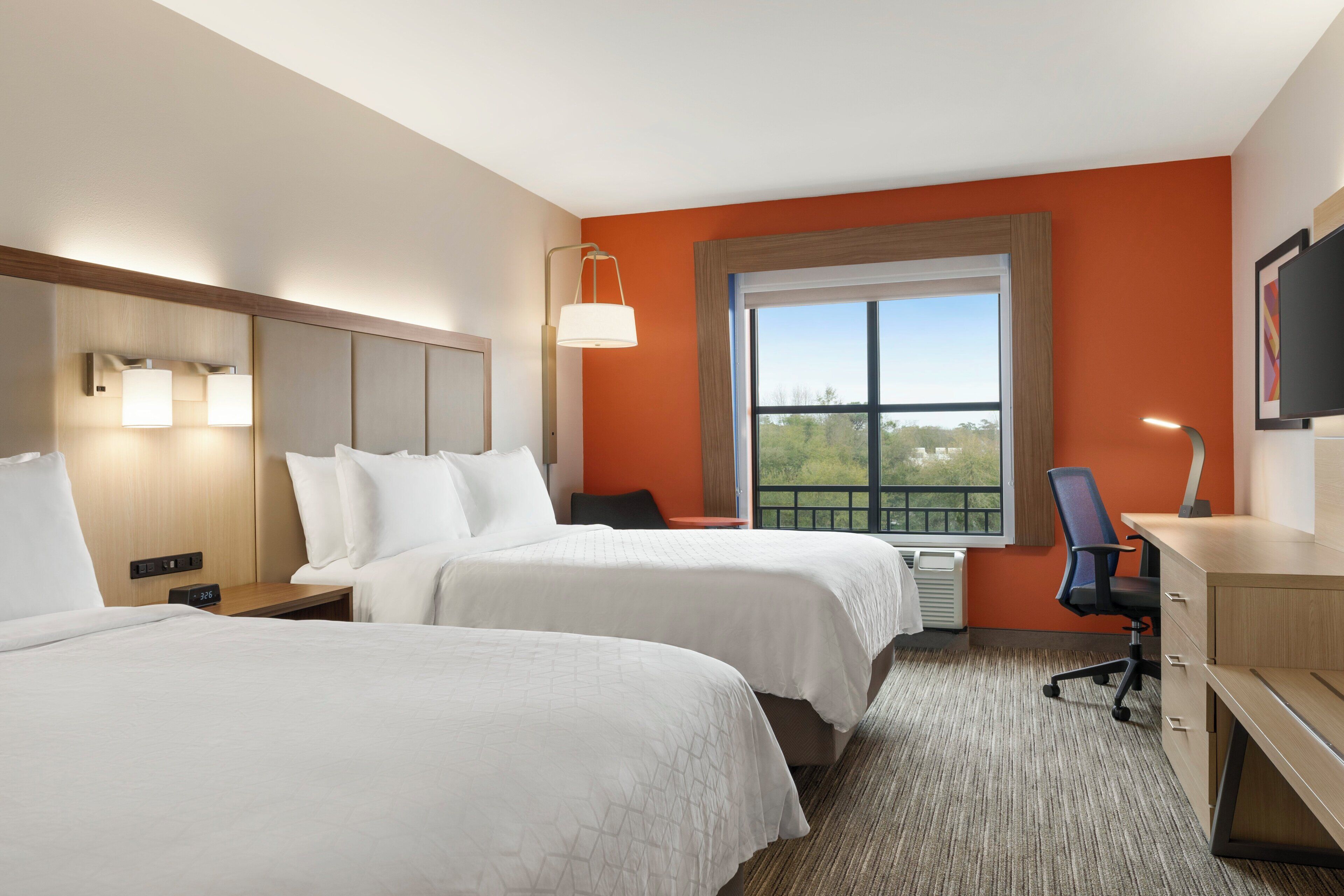 A hotel room with two beds, a desk, a chair, a TV, and a window with a view.