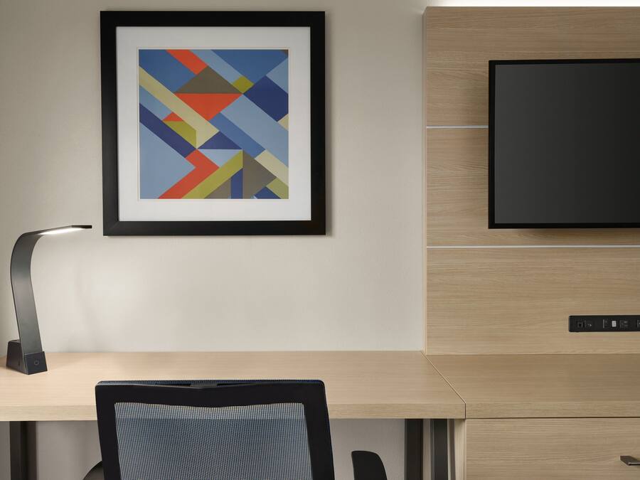 A modern office desk with a computer monitor, a framed abstract artwork, and a chair.
