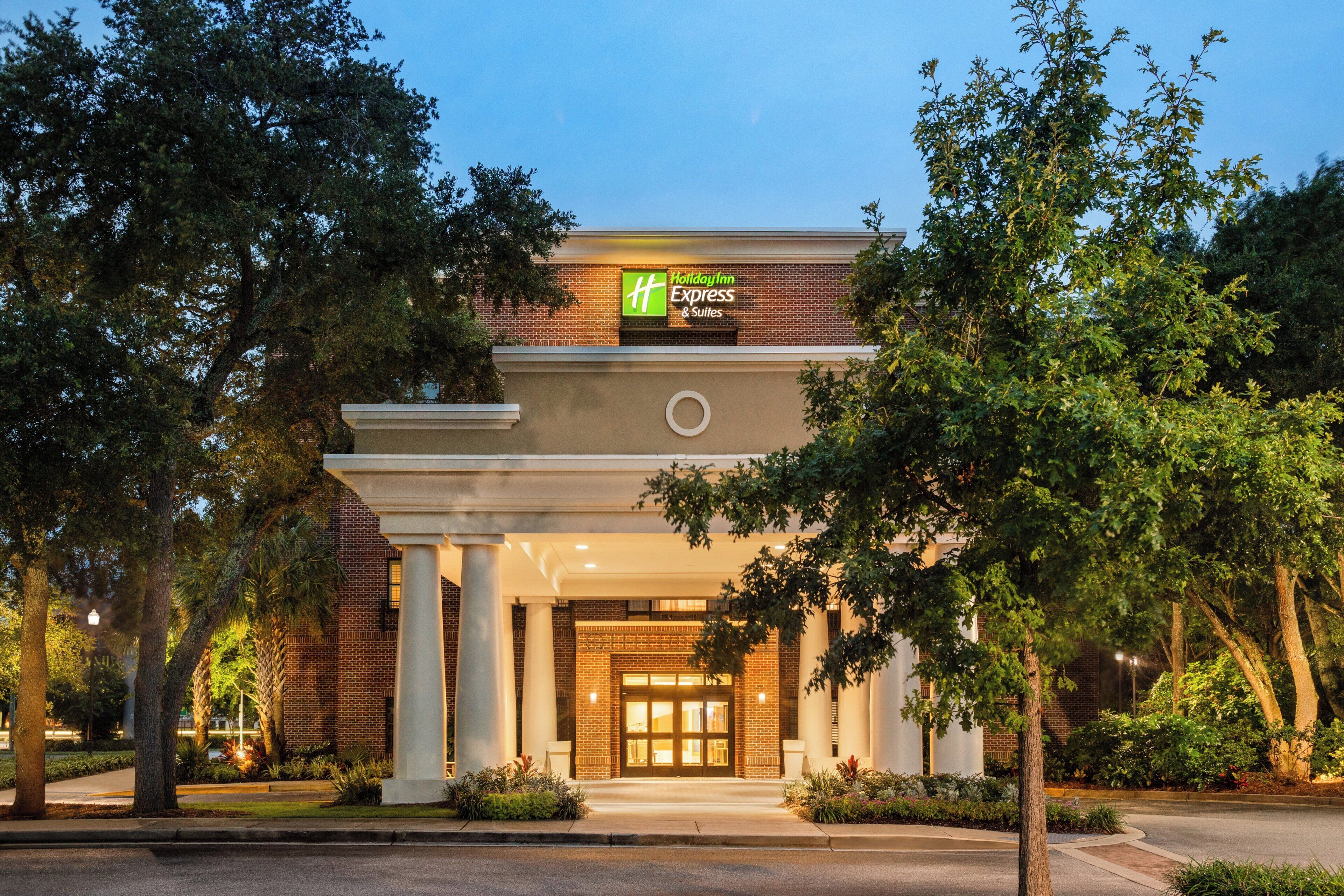 L’entrée d’un hôtel Holiday Inn Express & Suites, avec une façade en briques, de grandes colonnes et un hall d’entrée bien éclairé.
