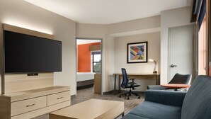 A modern hotel room with a flat-screen TV, a wooden dresser, a blue sofa, a desk with a chair, and a painting on the wall. - Holiday Inn Express & Suites Mt. Pleasant by IHG (Mount Pleasant)