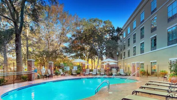 A swimming pool with lounge chairs and umbrellas, surrounded by trees and a building with multiple windows. - Holiday Inn Express & Suites Mt. Pleasant by IHG (Mount Pleasant)