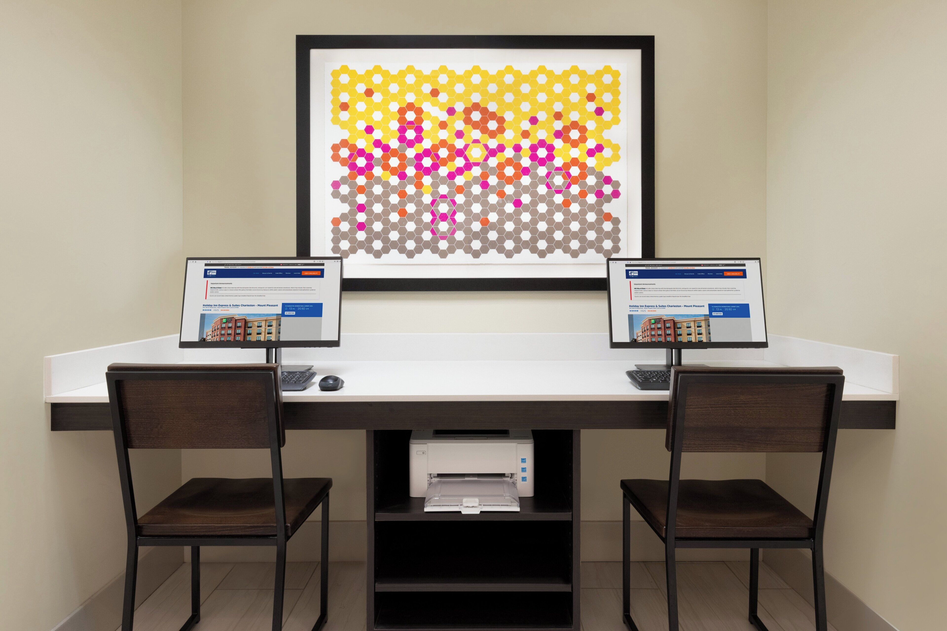 A workspace with two monitors, a framed abstract art piece, and a printer on a desk.