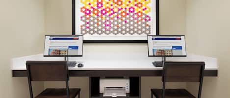 A workspace with two monitors, a framed abstract art piece, and a printer on a desk.