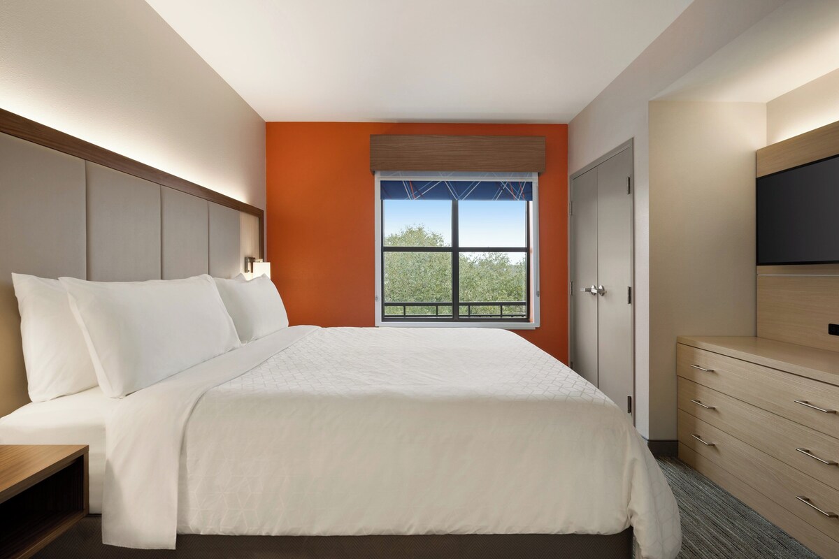 A hotel room with a bed, a dresser, a television, and a window with a view.