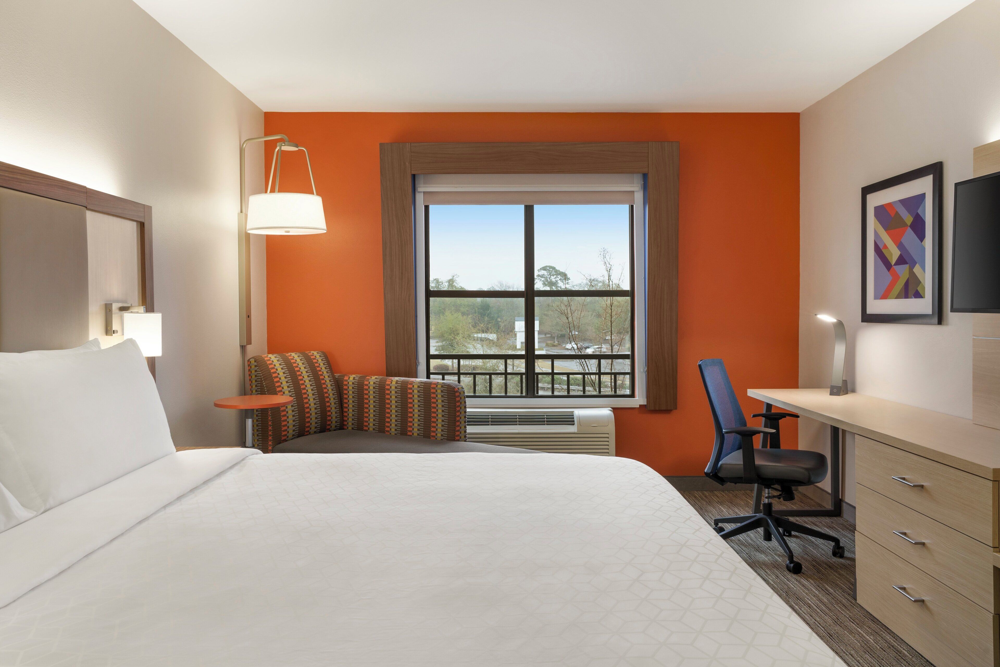 Habitación de hotel con cama, escritorio, silla, ventana con vistas y televisión.