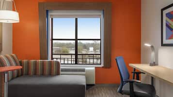 A hotel room with a bed, a desk, a chair, a window with a view, and a lamp.