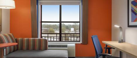 Habitación de hotel con cama, escritorio, silla, ventana con vistas y lámpara.