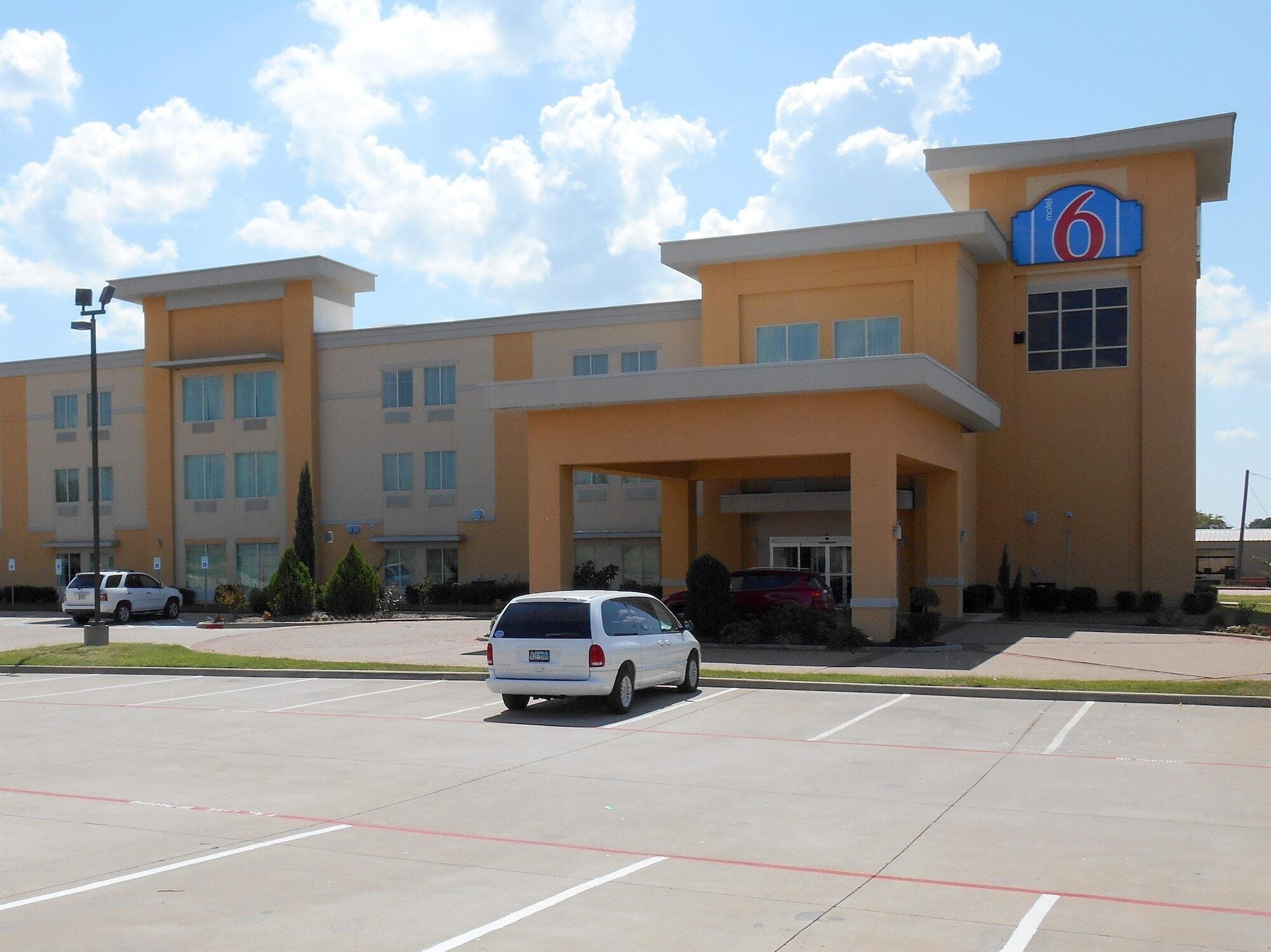 A motel with a large parking lot, a central entrance, and a sign indicating it is the 6th motel.