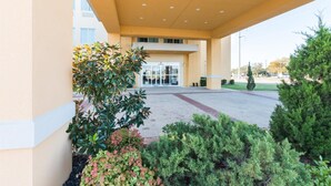 A building entrance with a covered walkway, glass doors, and surrounding greenery. - Motel 6 Joshua, TX (Joshua)