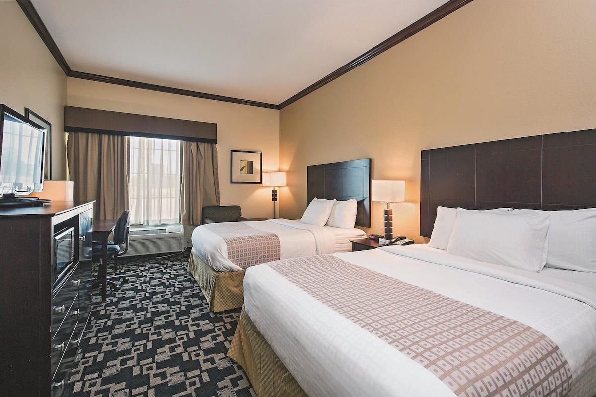 A hotel room with two beds, a desk with a computer, and a window with curtains.