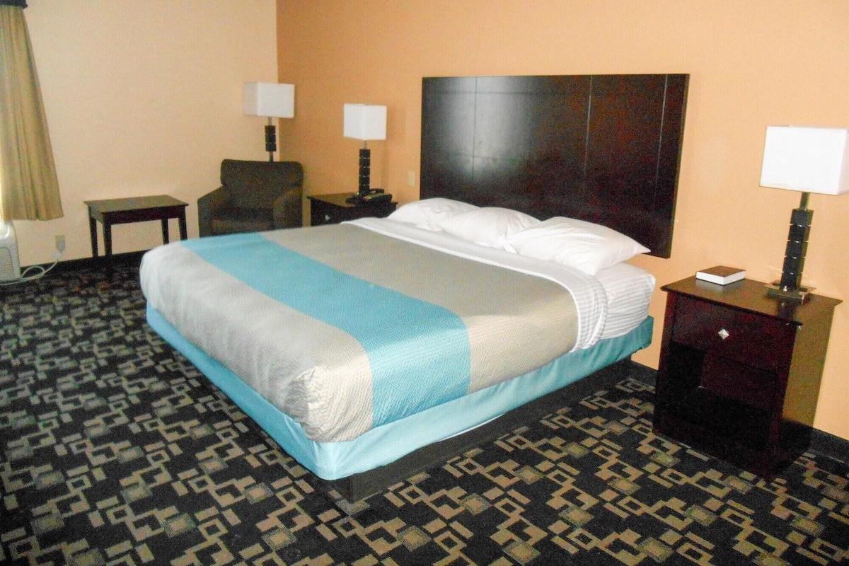 A hotel room with a large bed, two bedside tables, a chair, and a lamp.