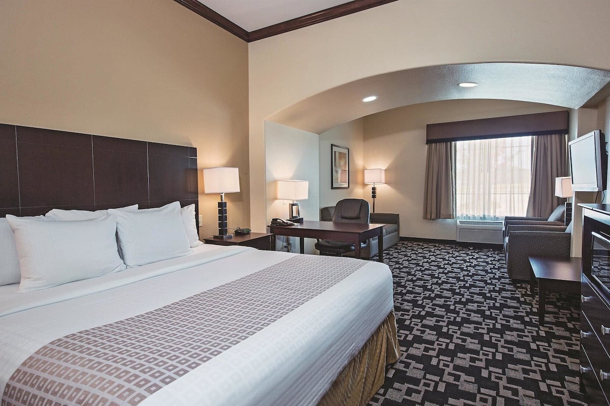A hotel room with a large bed, a desk, a chair, a television, and a window with curtains.