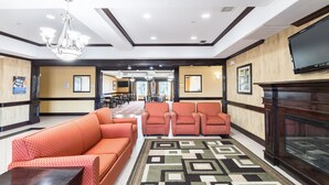 A hotel lobby with a patterned carpet, orange sofas, a TV, and a fireplace. - Motel 6 Joshua, TX (Joshua)