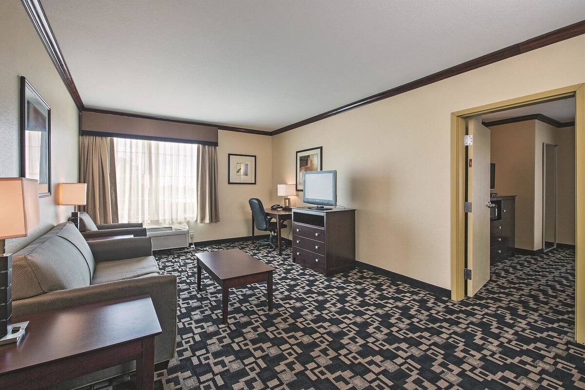 A hotel room with a sofa, a desk with a computer, a chair, a lamp, and a patterned carpet.