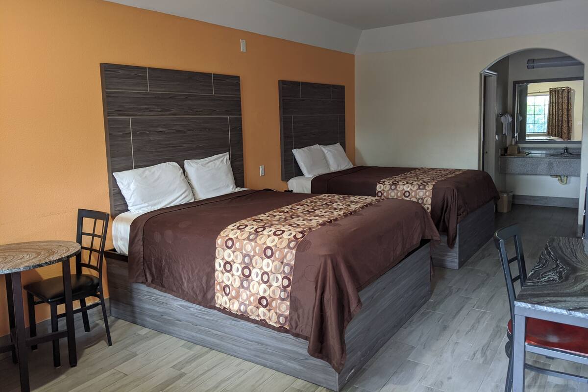 A hotel room with two beds, a small table, and a chair.
