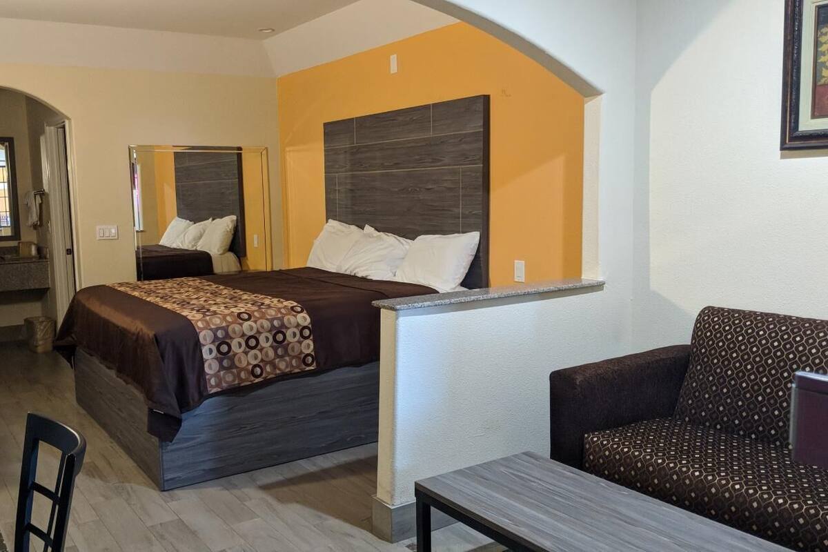 A hotel room with a bed, a sofa, a table, and a mirror.