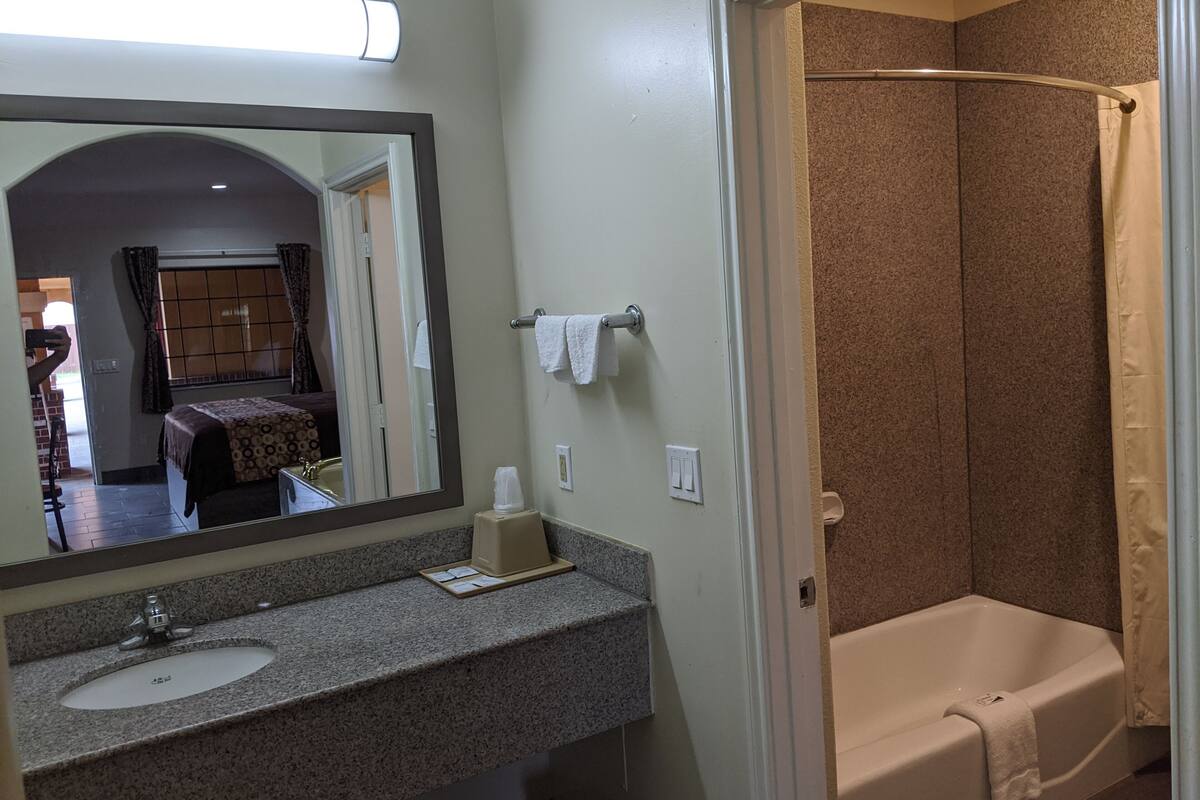 A bathroom with a sink, mirror, towel rack, and shower area.