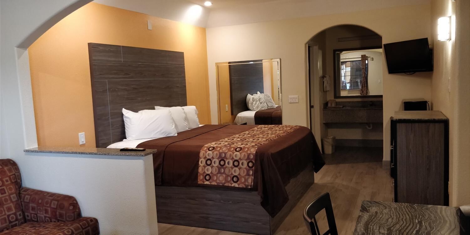 A hotel room with a bed, a desk, a chair, a TV, and a bathroom visible through an archway.