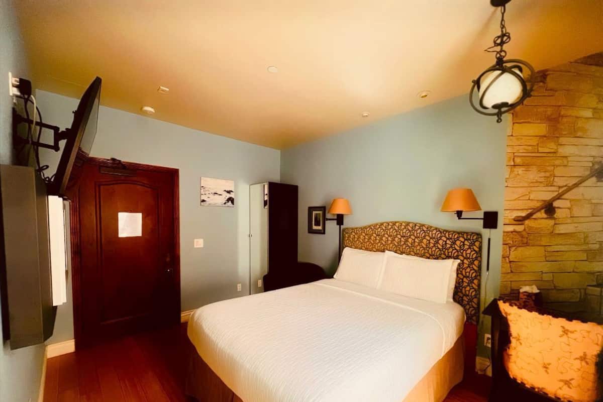 Quarto com uma cama grande, porta de madeira, guarda-roupa, escrivaninha e parede de pedra.