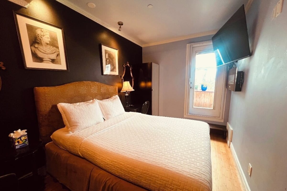 Quarto com cama grande, mesa de cabeceira, abajur, televisão e quadros nas paredes.
