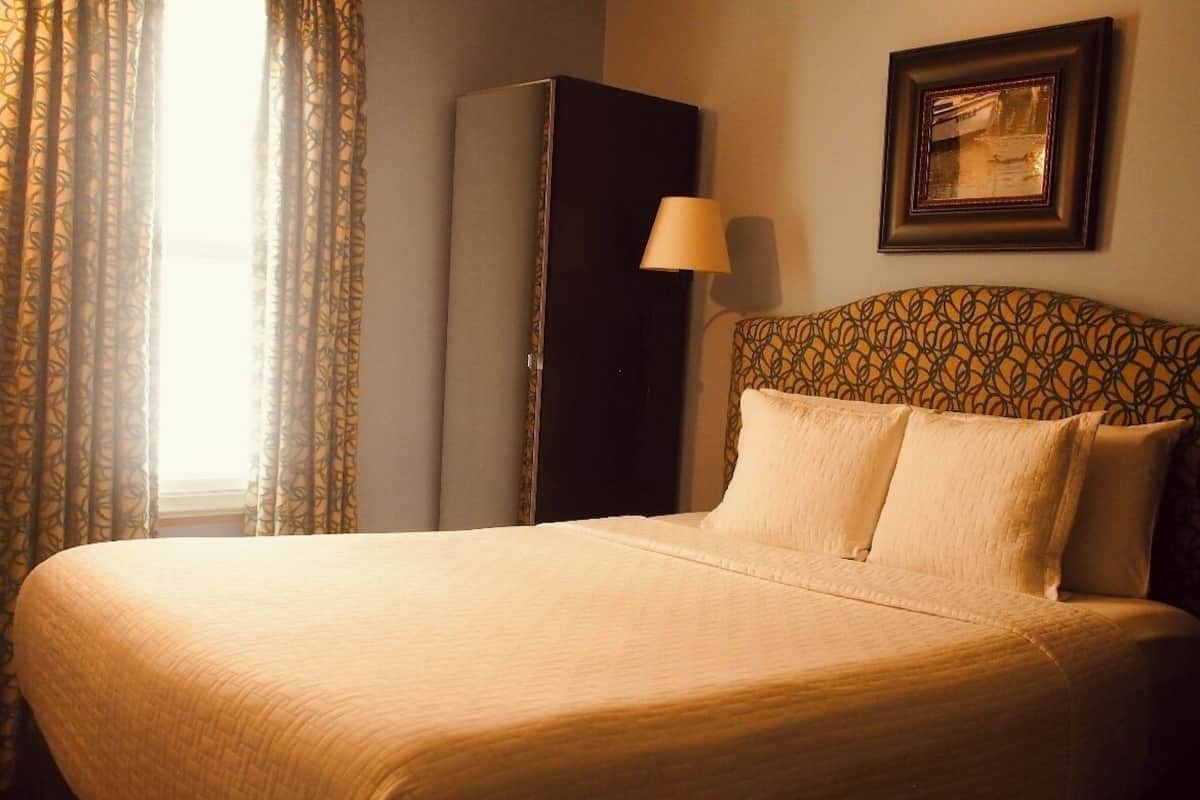 Quarto de hotel com uma cama grande, um guarda-roupa, um abajur e um quadro na parede.