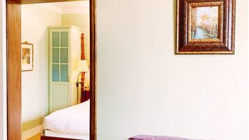 A room with a wooden bed, a purple armchair, a framed picture on the wall, and a door leading to another room.