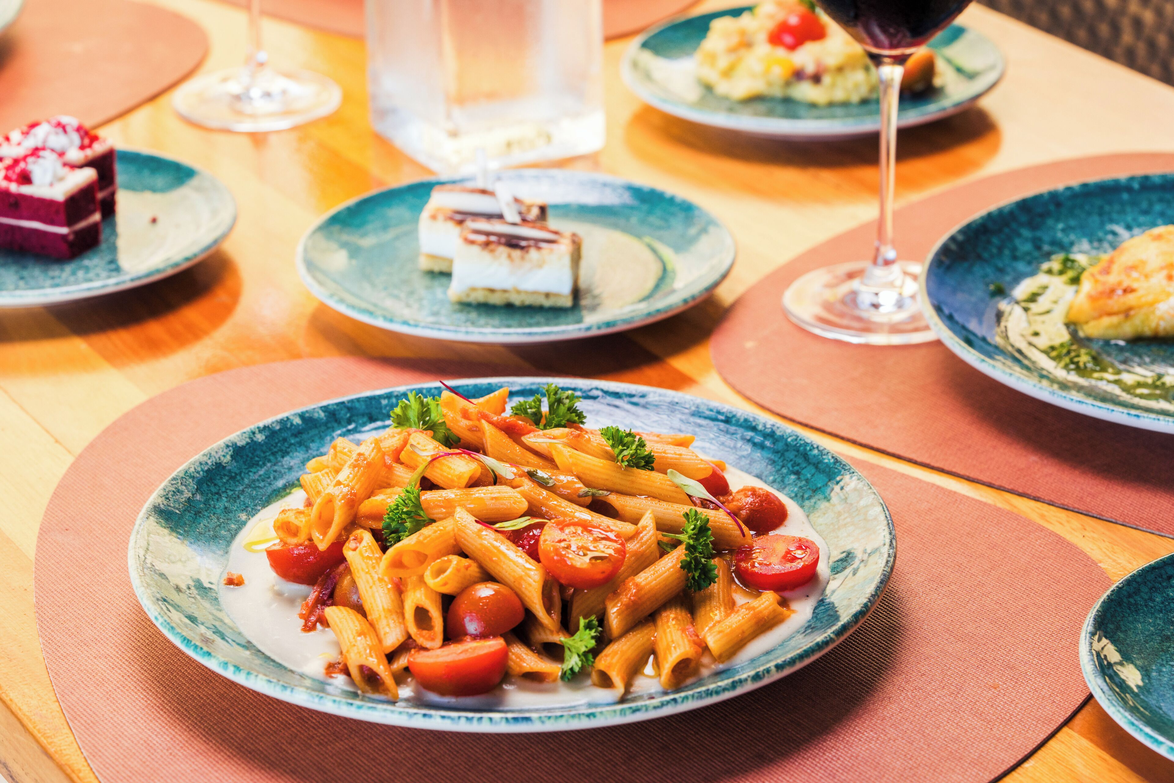 A dining table with plates of pasta, a glass of red wine, and a water glass.