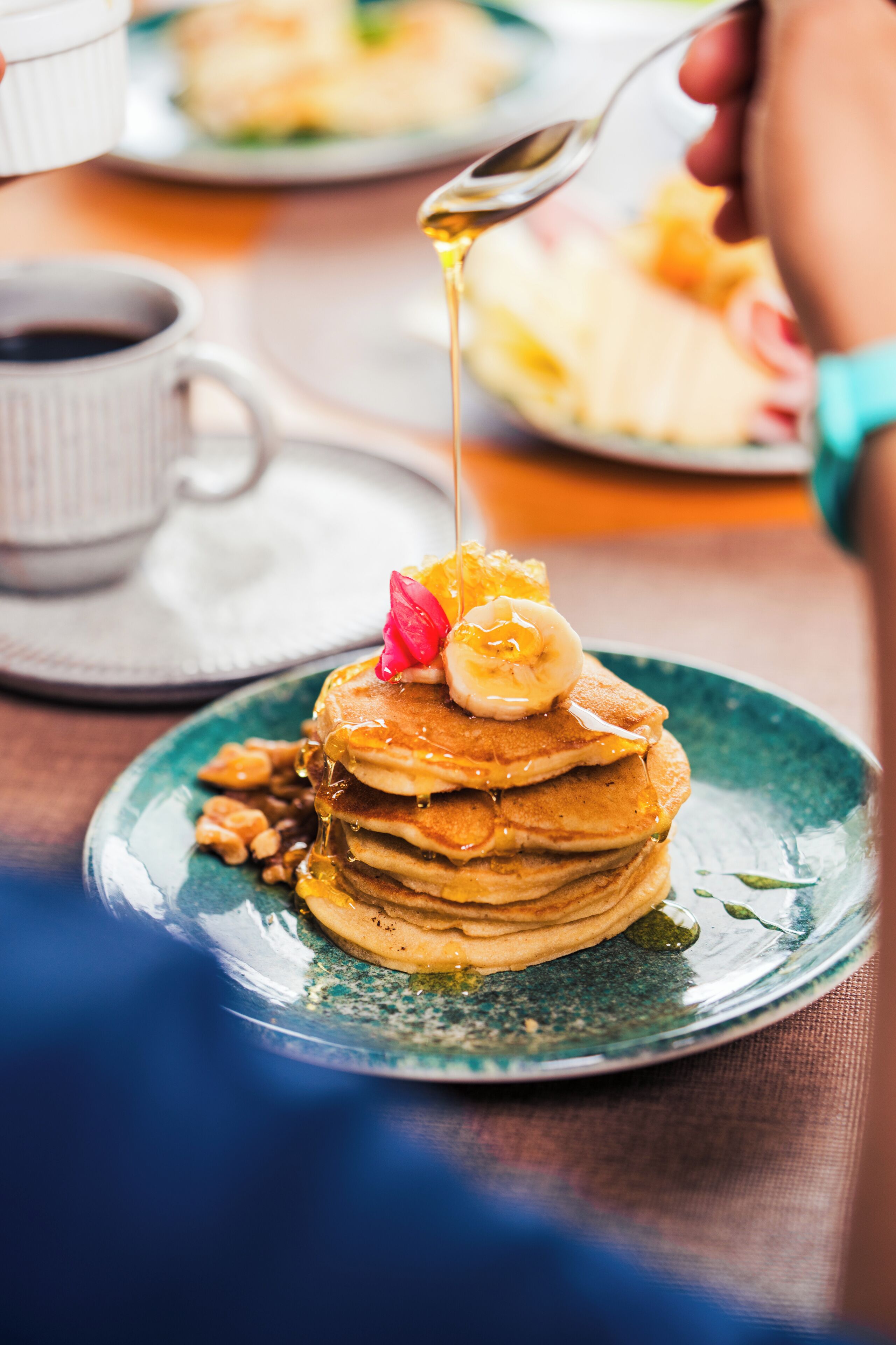 Une pile de crêpes nappées de sirop, garnies de rondelles de banane, sur une assiette.