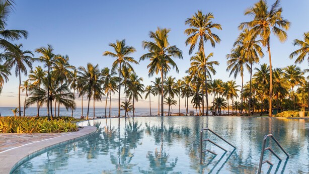 A pool with clear blue water, surrounded by palm trees and a view of the ocean. - Sauipe Brisa Grand Premium – All Inclusive (Mata de São João)