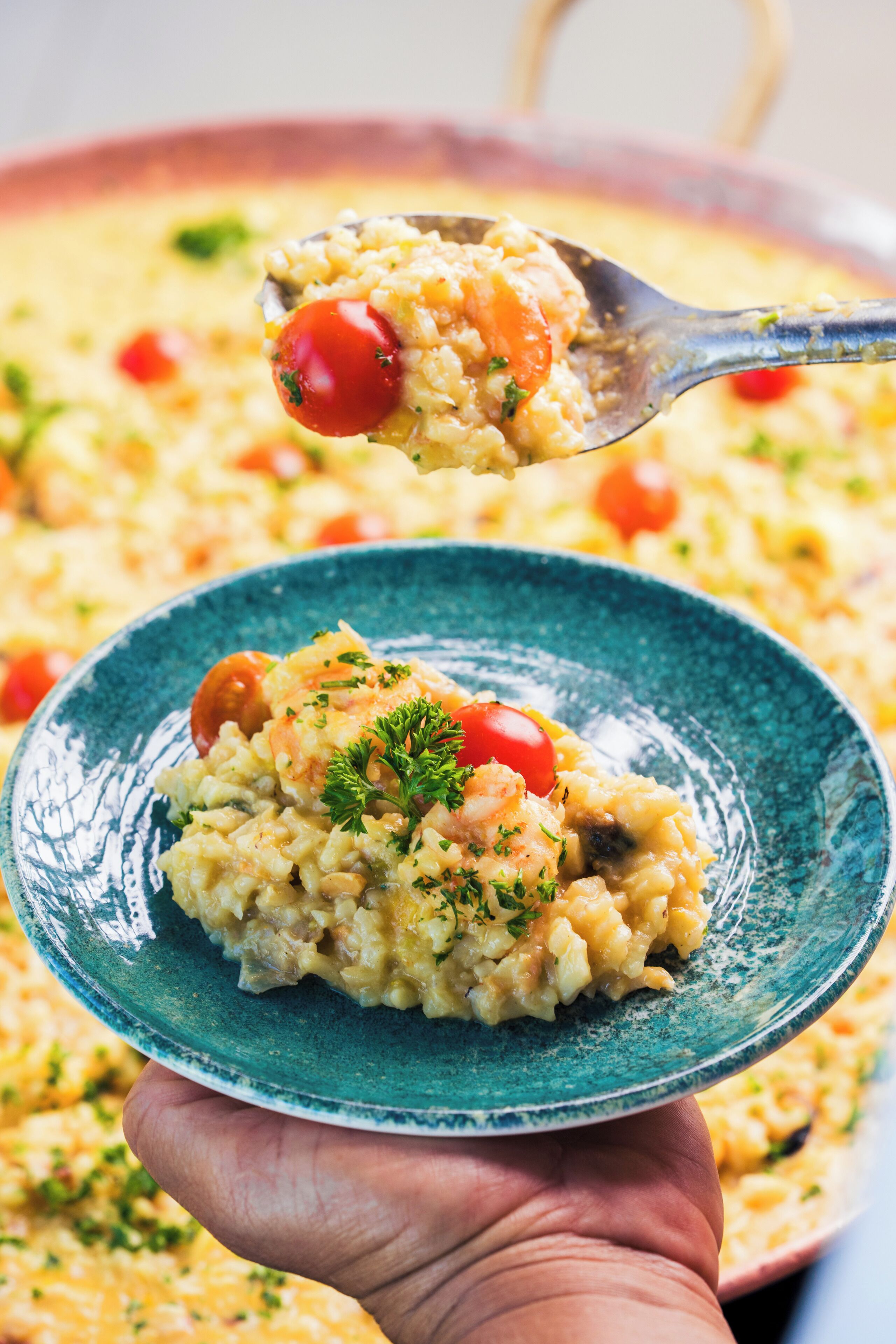Una mano tiene un cucchiaio di risotto con pomodorini e prezzemolo.