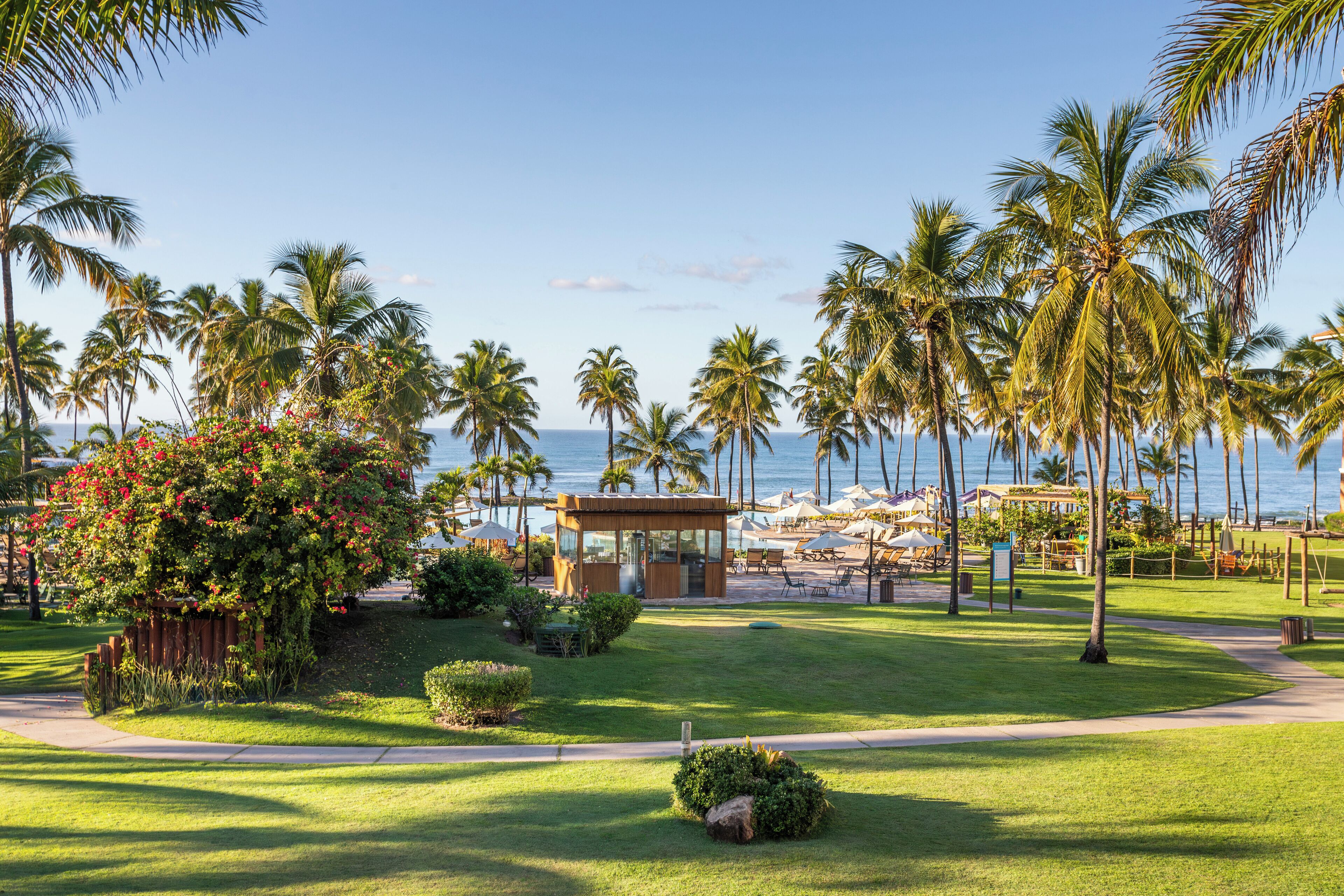 A resort with a beach view, palm trees, and a covered seating area.