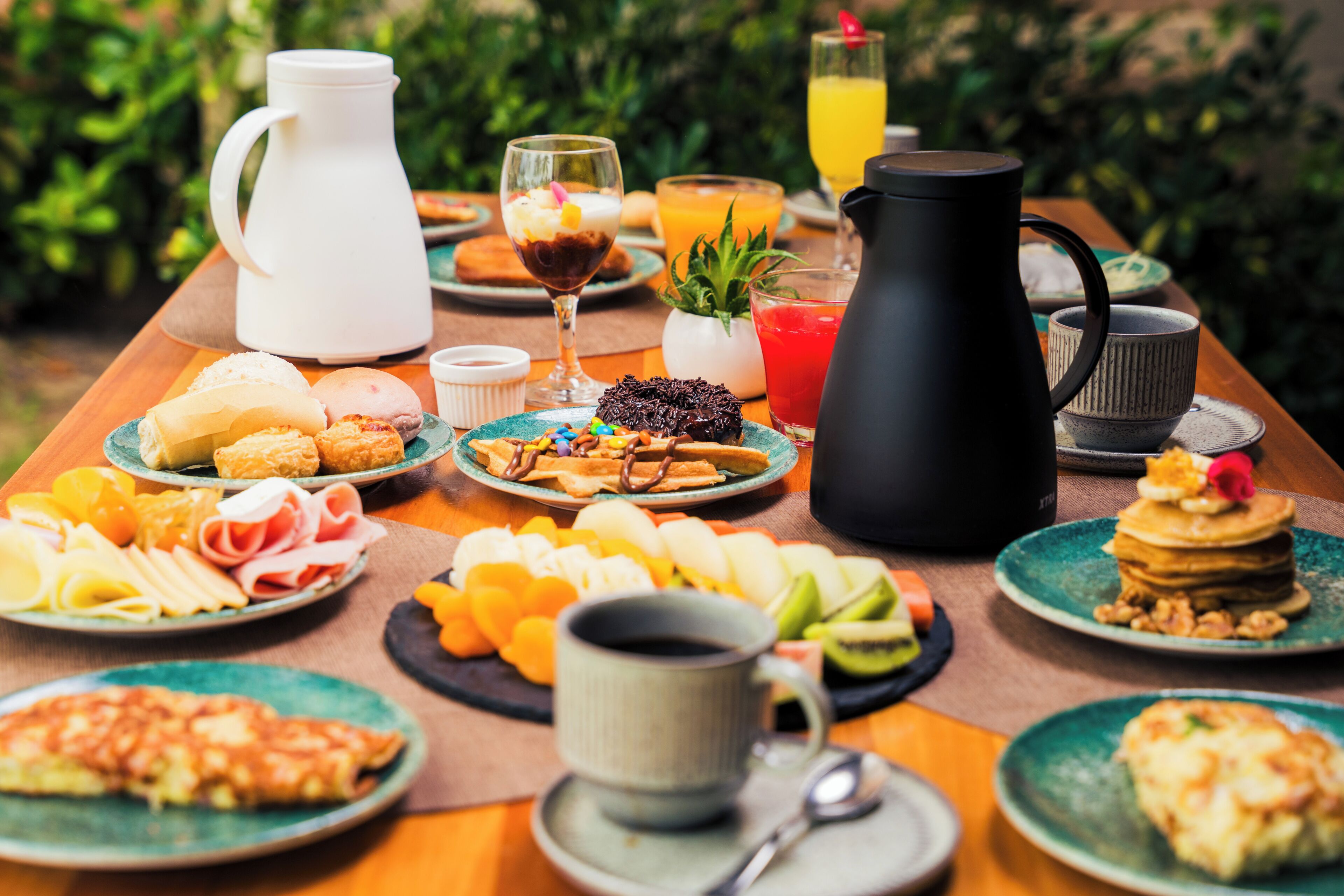 Una mesa de desayuno con diversos alimentos, una taza de café, una jarra y un vaso de jugo de naranja.