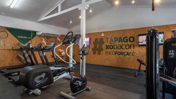 A gym with exercise equipment, a wooden wall with a logo, and a ceiling with lights.