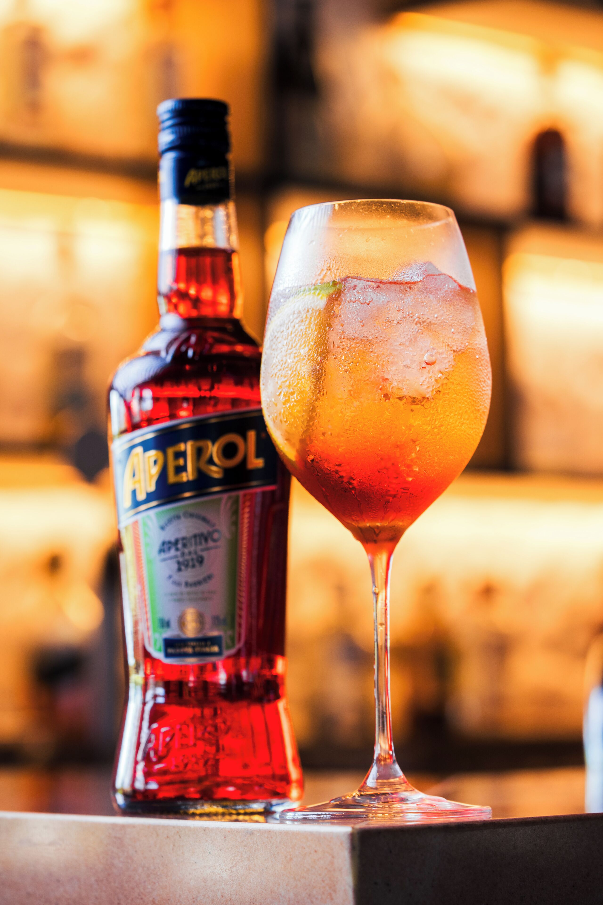 A bottle of Aperol and a glass of cocktail on a bar counter.