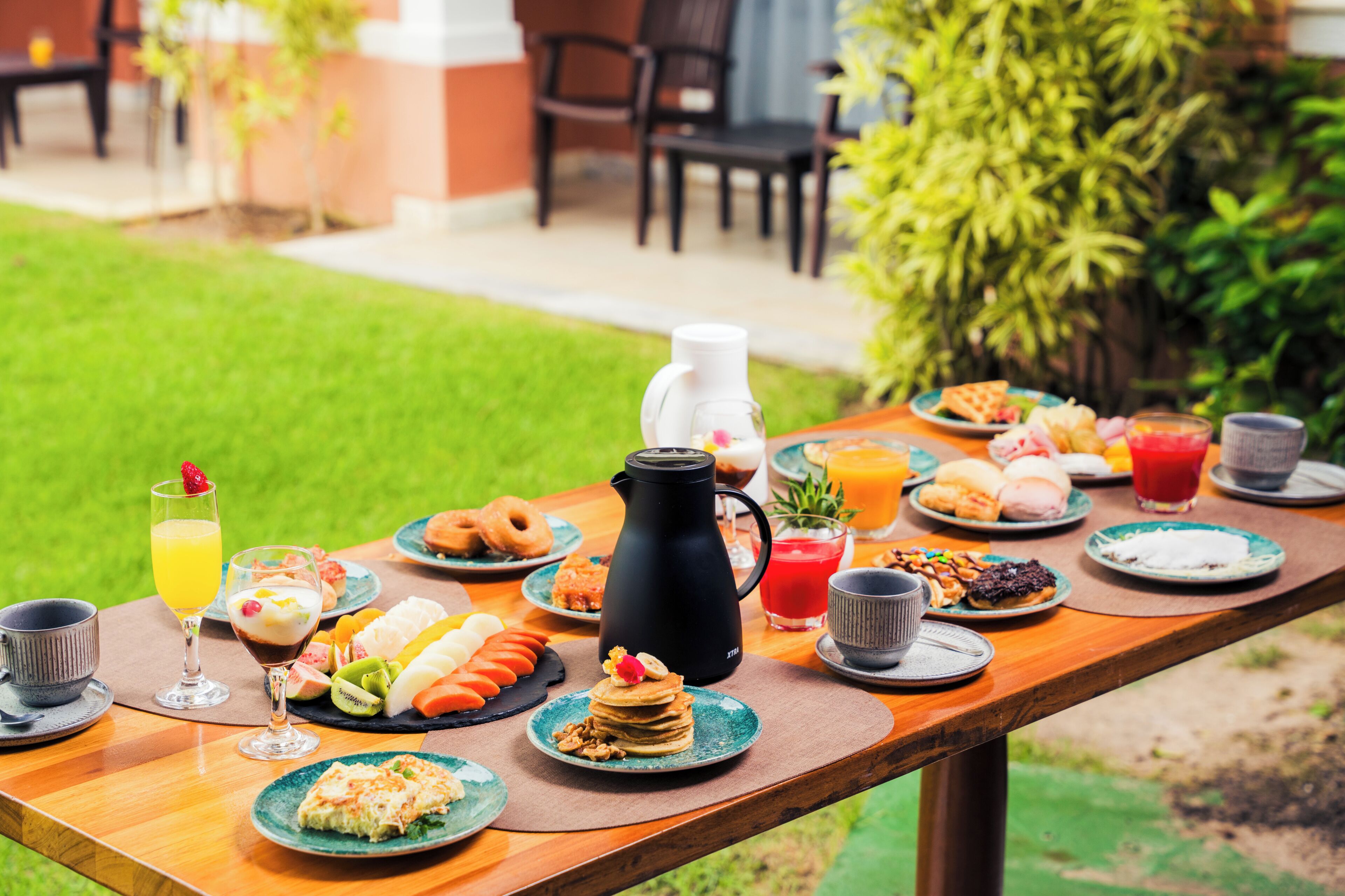 Un coin petit-déjeuner aménagé à l’extérieur, avec divers aliments et boissons disposés sur une table en bois.
