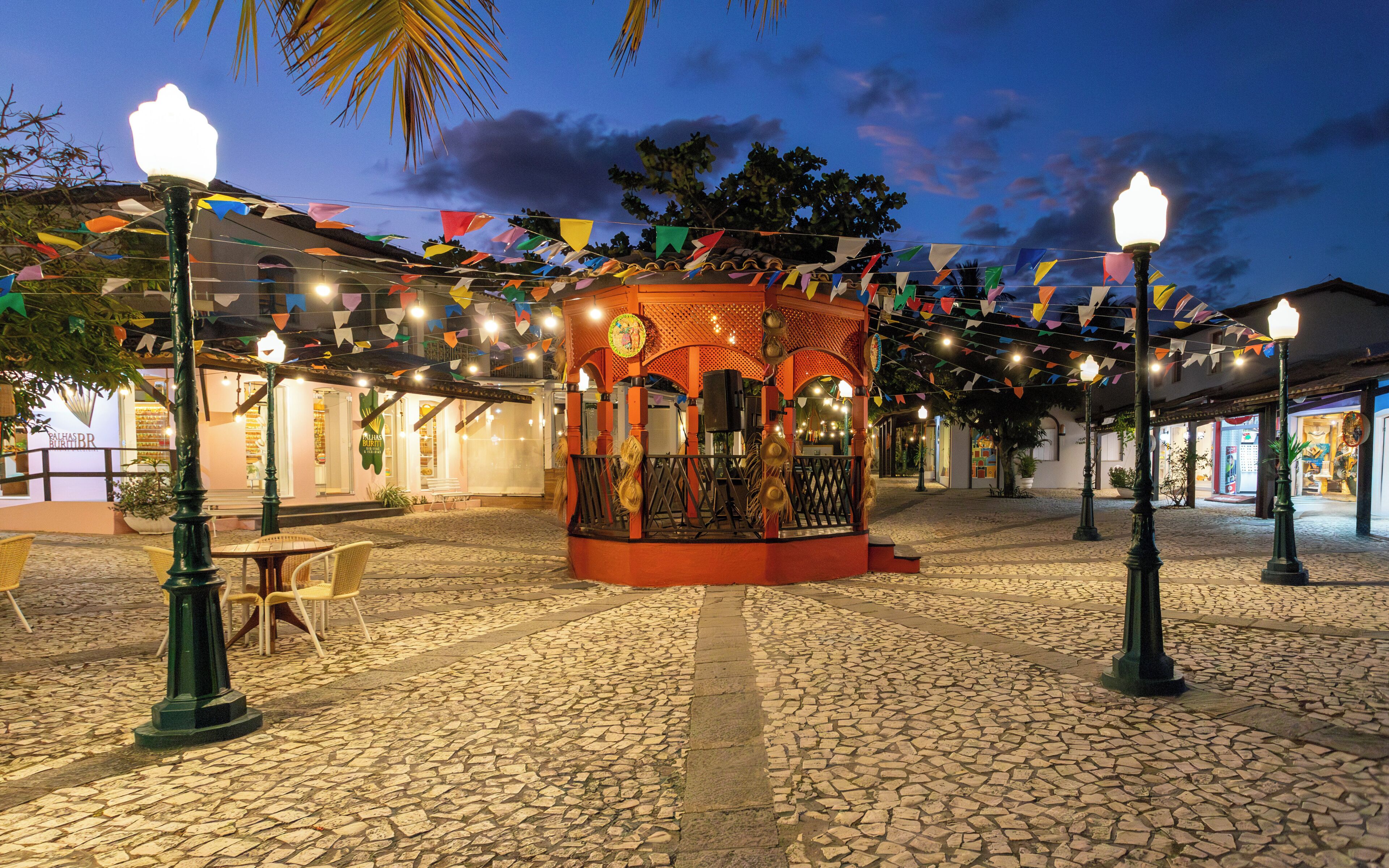 A cobblestone plaza with a gazebo, street lamps, and colorful flags.