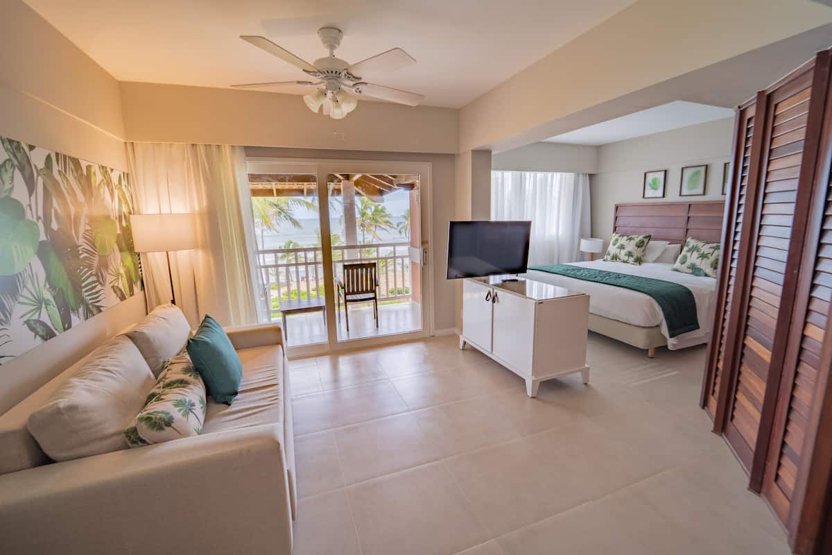 A hotel room with a balcony, a TV, a bed with a green bedspread, and a ceiling fan.