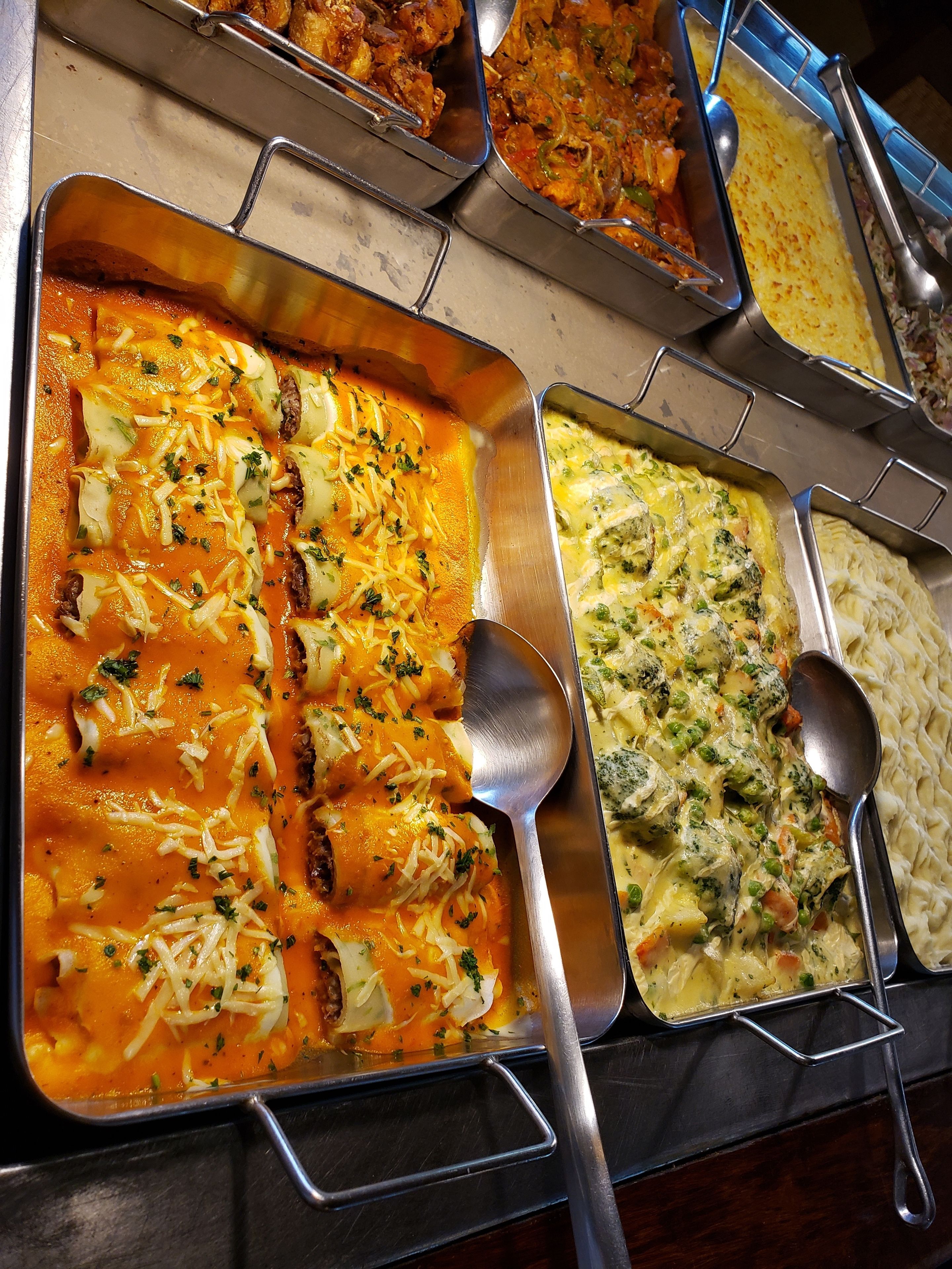 A buffet with various dishes including enchiladas, a casserole with broccoli and cheese, and a pasta dish.