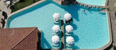 An aerial view of a swimming pool with multiple umbrellas and lounge chairs.