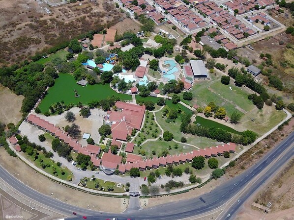 Vista aérea de una zona residencial con piscina, áreas verdes y una carretera.