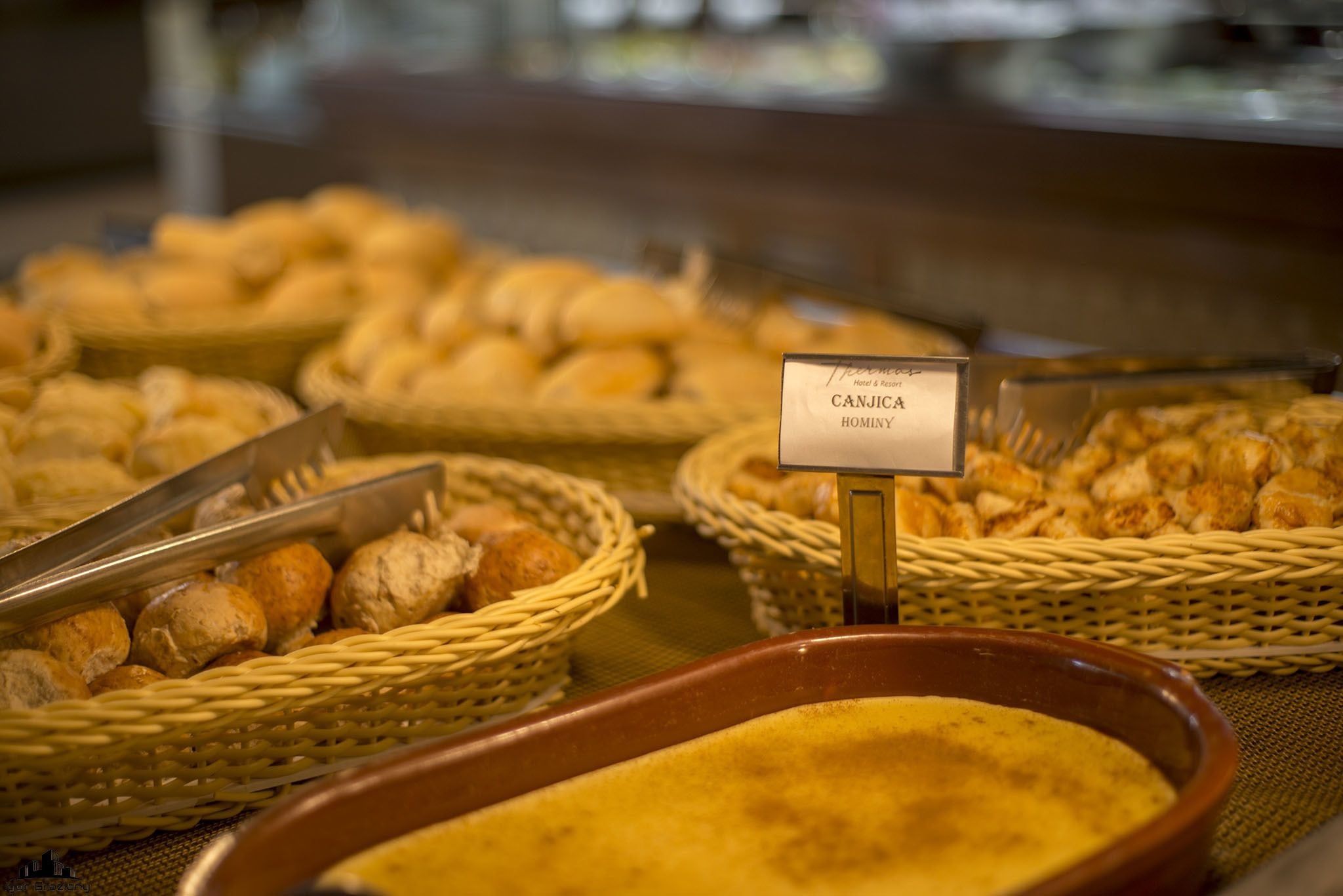 Un bufé con diversas opciones de productos horneados, como pan y pasteles, exhibidos en cestas de mimbre y un recipiente de cerámica.